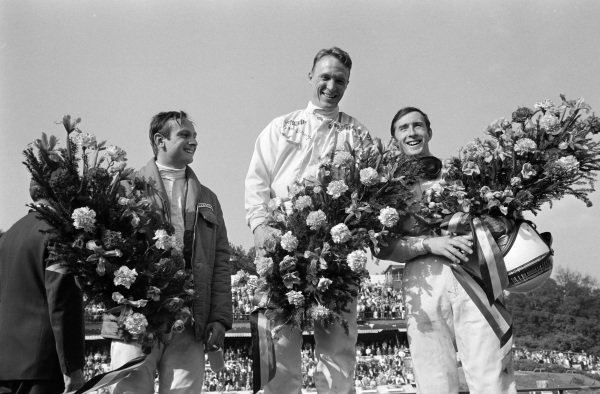 Dan Gurney, 1st position, Jackie Stewart, 2nd position, and Chris Amon, 3rd position, celebrate on the podium.